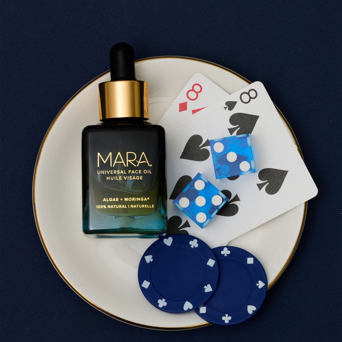 MARA Universal Face Oil on a plate with playing cards and poker chips depicting 8 on a dark background