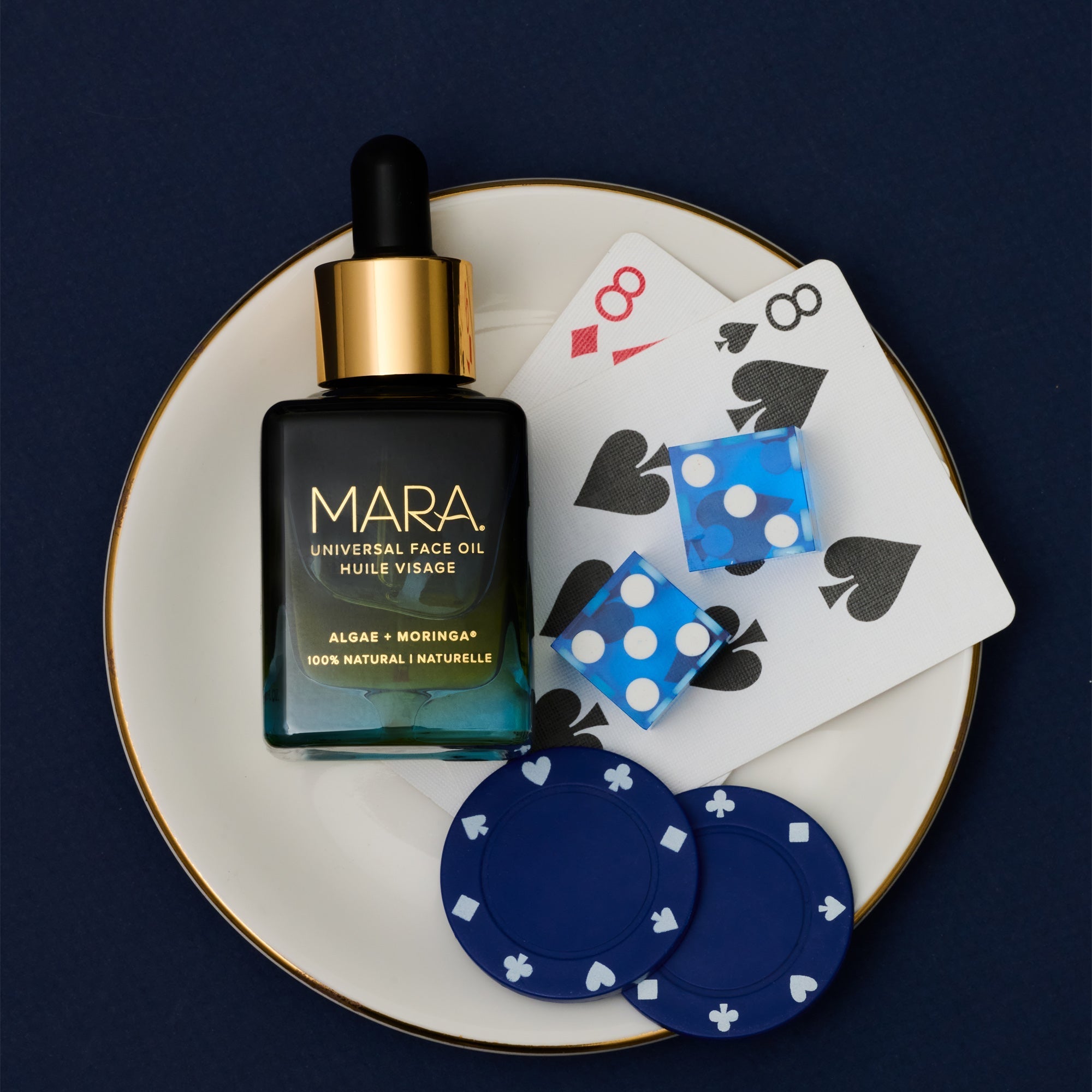 MARA Universal Face Oil on a plate with playing cards and poker chips depicting 8 on a dark background