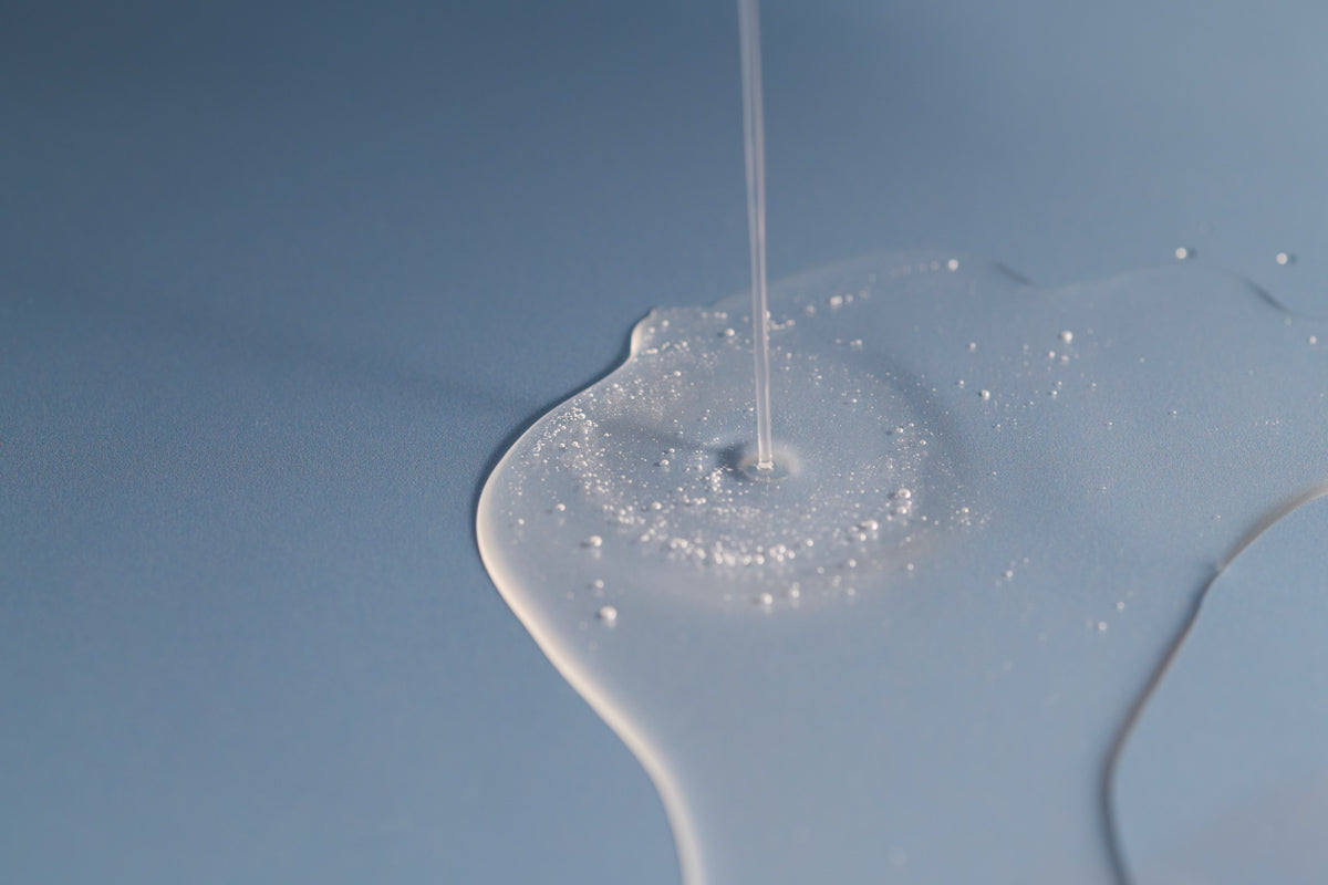 close up of Algae Enzyme Cleansing Oil pouring on blue surface