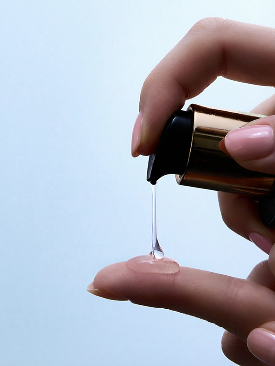 hand pumping Aura Cleanse Foaming Gel Cleanser on finger on blue background