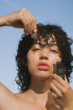 Woman holding a dropper and Algae Retinol Face Oil against a blue sky