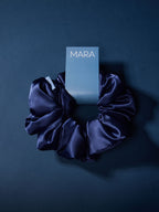 A navy jumbo scrunchie tag that reads 'MARA' against a dark navy background.