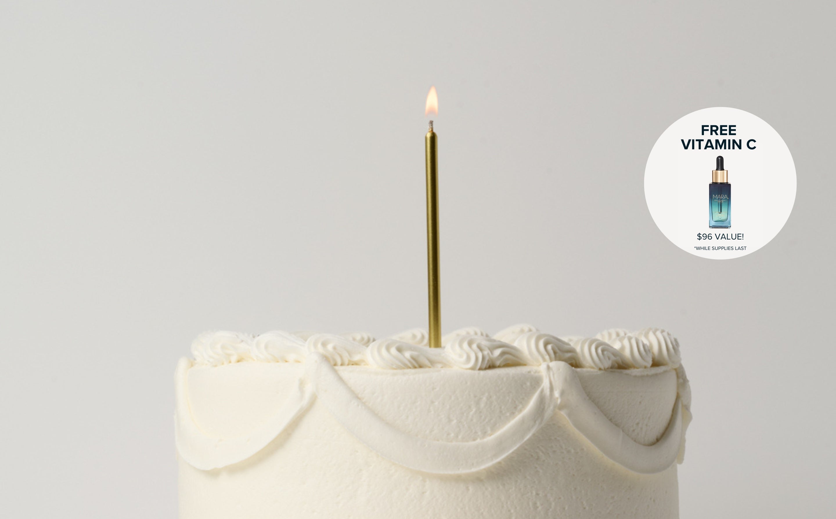 White cake with a lit gold candle on a gray background, featuring a free vitamin C serum offer.