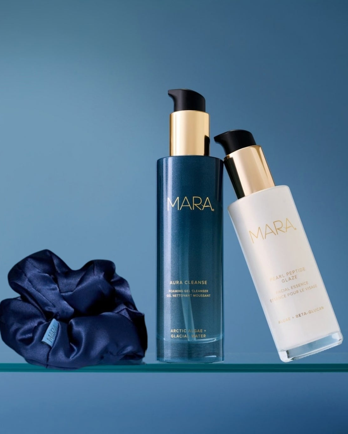 Aura Cleanse Gel Cleanser, Pearl Peptide Glaze, and Navy scrunchie on glass shelf with blue background