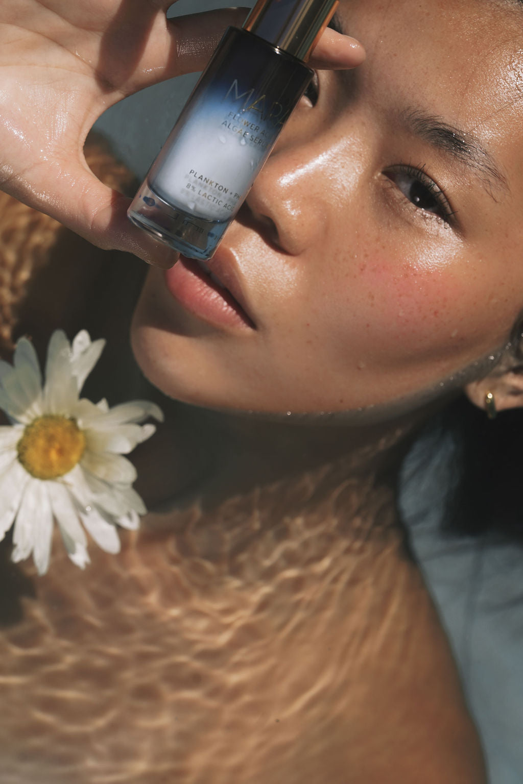 Woman with glowing skin holding MARA Flower Acid Algae Serum