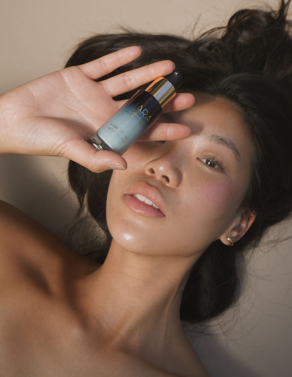 Woman holding Flower Acid Algae Serum near her face against a neutral background