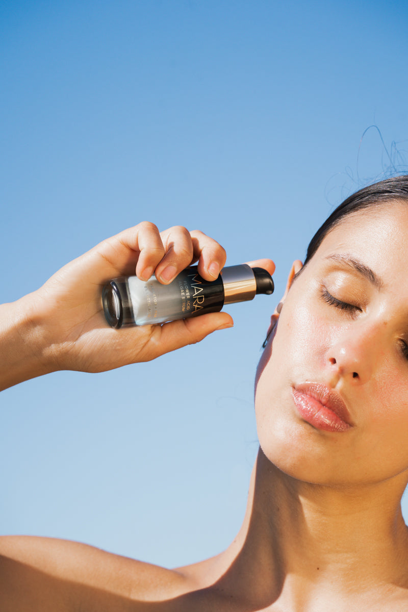 Person applying Flower Acid Algae Serum against a clear blue sky