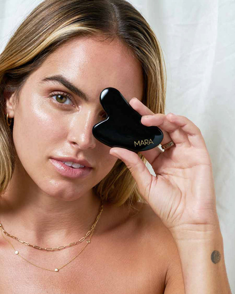 Model holding Gua Sha tool in front of eye