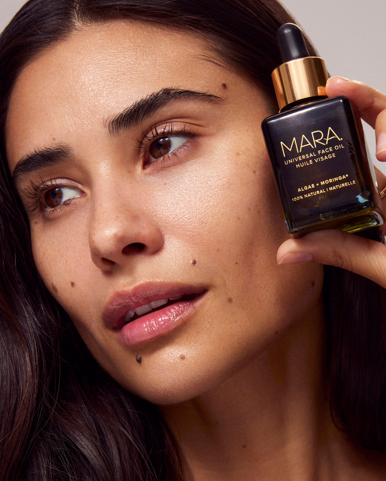 Woman holding Universal Face Oil in hand near face 