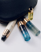 Deluxe Pearl Peptide, Cleansing Oil, Gel Cleanser, Universal Oil arranged on a white surface next to a black textured pouch.