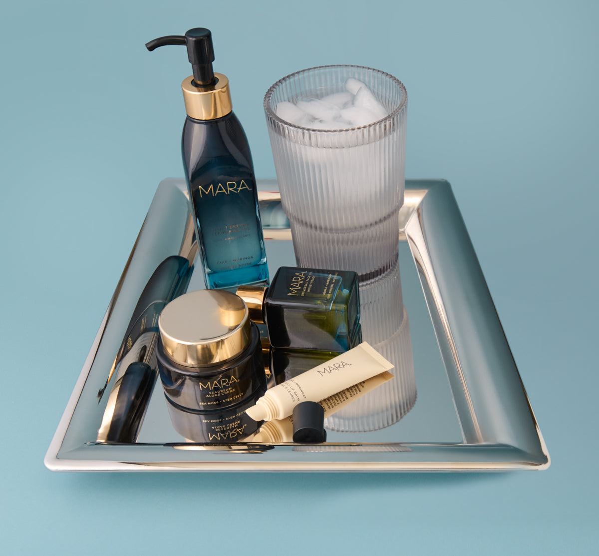 Cleansing Oil, SeaDream Algae Creme, Universal Face Oil and Sea Silk Lip Balm on a silver tray with a glass of water