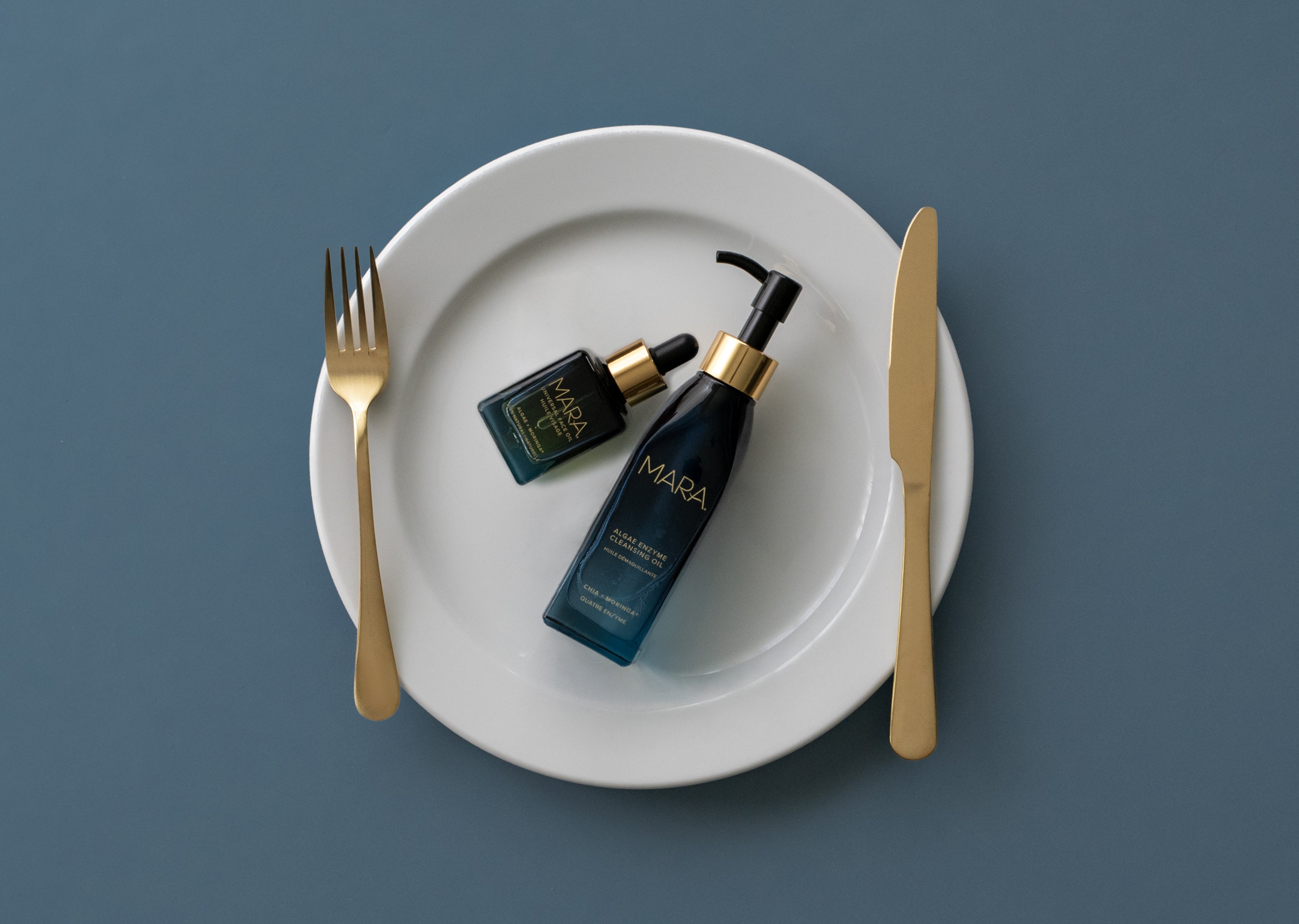 Algae Enzyme Cleansing Oil and Universal Oil on white plate on blue surface
