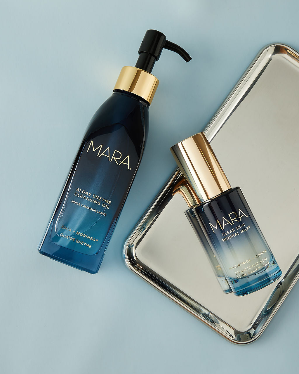 Cleansing Oil and Clear Skin Mineral Milk on silver tray on blue background