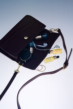 Black handbag with Deluxe Nighttime Kit, sunglasses, and earbuds spilling out on a light gray background