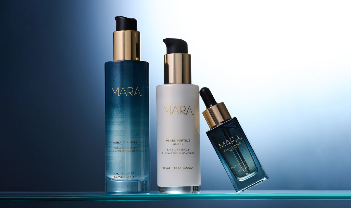 Aura Cleanse Gel Cleanser, Pearl Peptide Glaze, Sea Vitamin C Serum arranged on a glass shelp against a blue gradient background