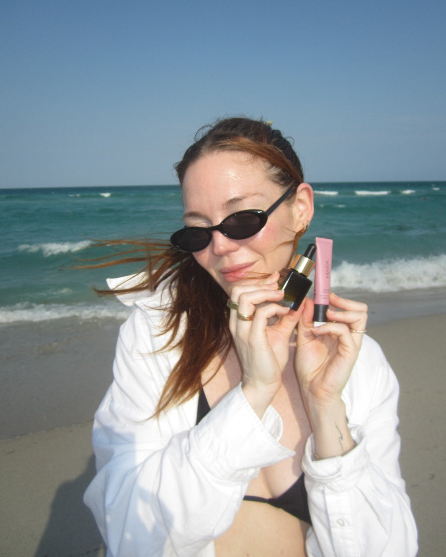 Allison holding Mini Universal Face Oil and Nude Beach Lip Balm at beach