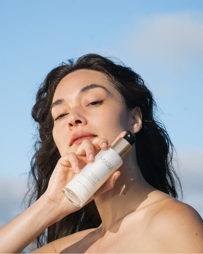 woman holding MARA Pearl Peptide Glaze in front of face with clear sky behind her