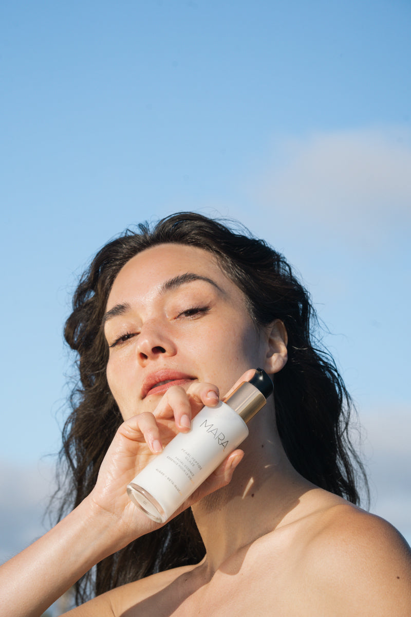 Woman holding Pearl Peptide Glaze with a clear blue sky in the background