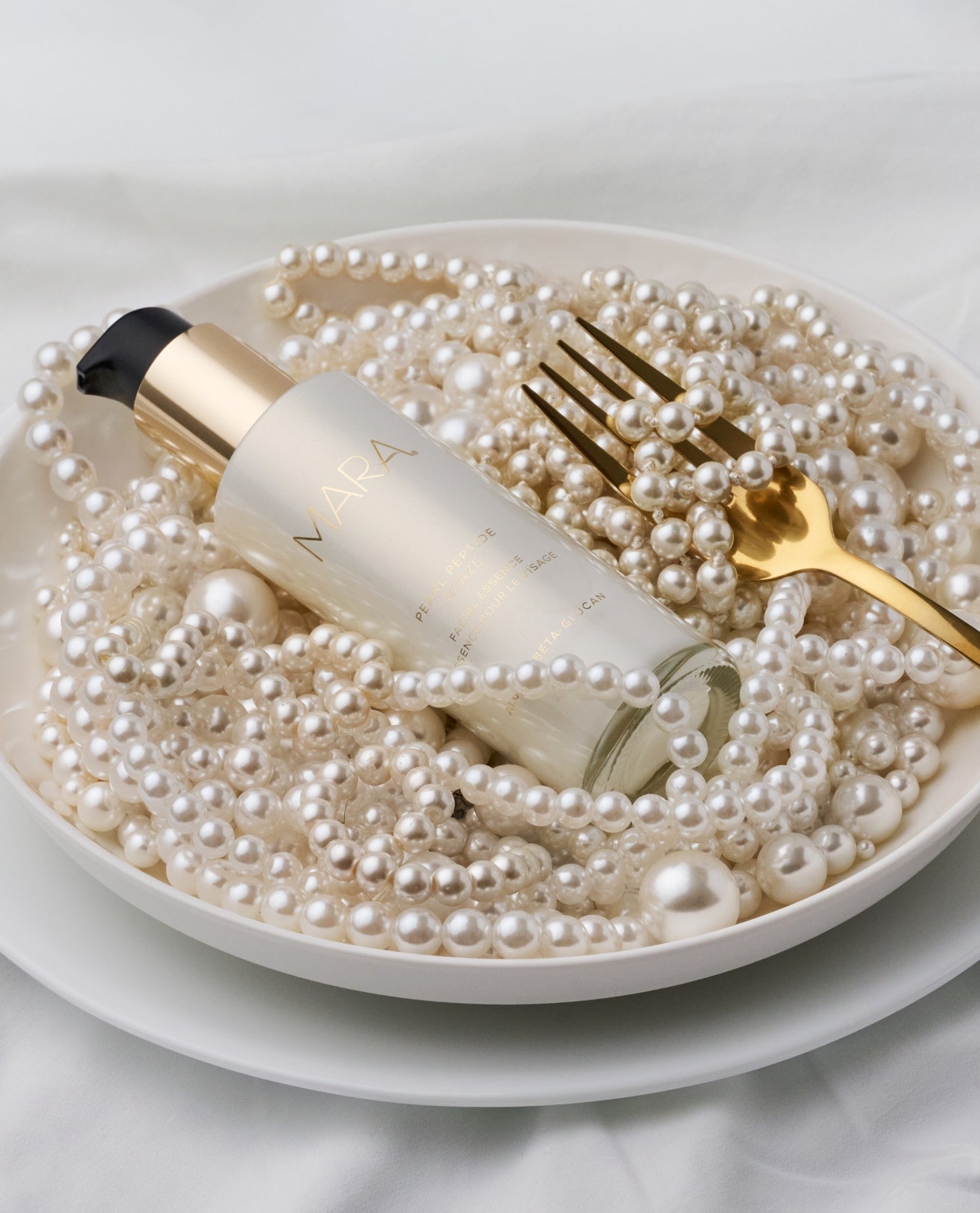 Pearl Peptide Glaze in a plate of pearls reminiscent of pasta with a gold fork