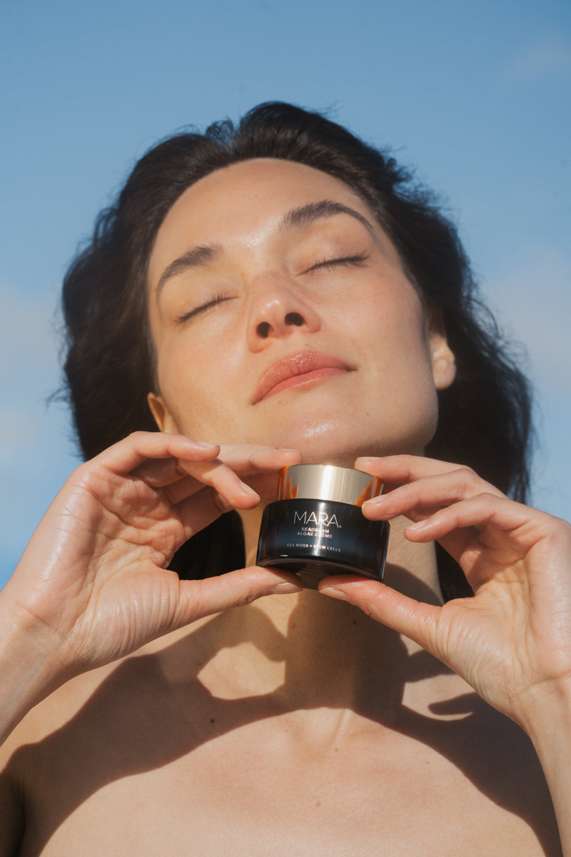 Woman holding a SeaDream Algae Creme against a clear blue sky.