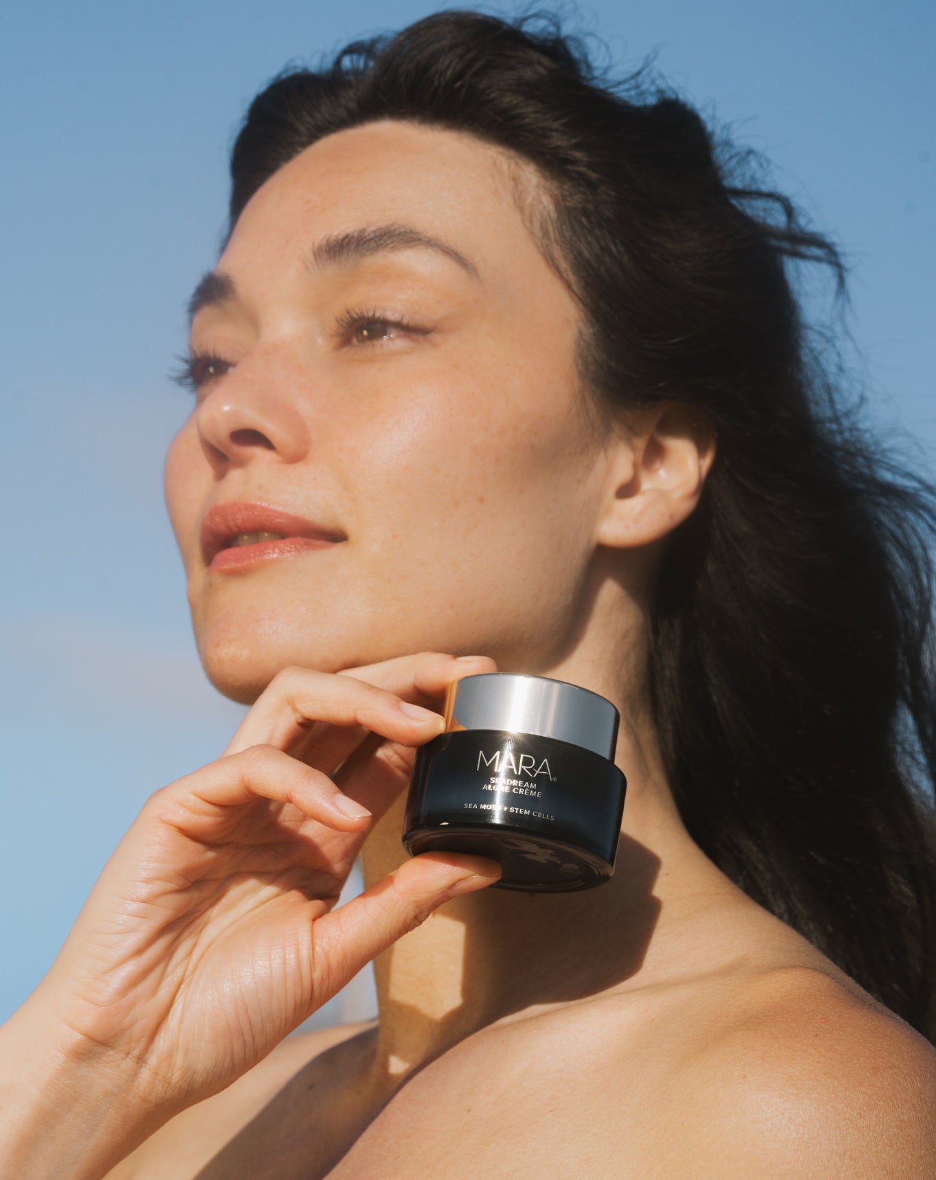 Woman holding a jar of SeaDream Algae Creme against a clear blue sky
