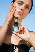 Woman holding Sea Kale Sunscreen Serum with a clear blue sky background