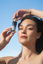 Person holding Sea Kale Sunscreen Serum against a clear blue sky
