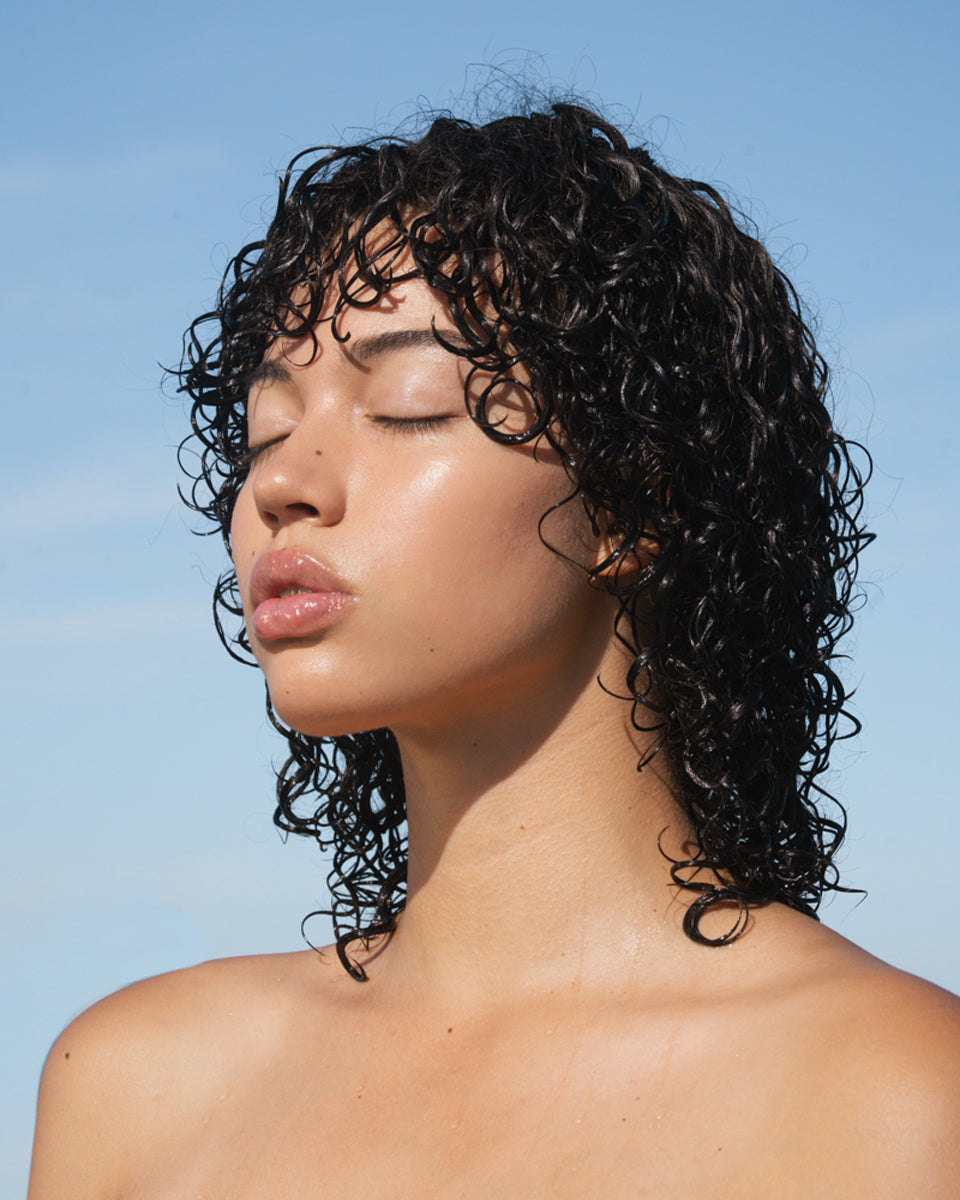 Model with curly hair and eyes closed with blue sky behind