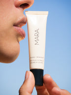 Tube of Clear Sea Silk Lip Balm held close to a person's lips against a blue background