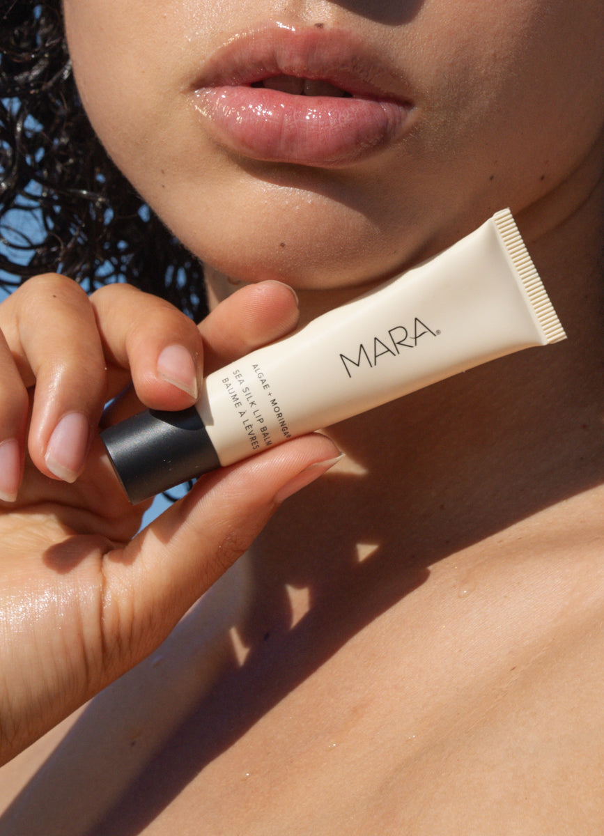 Hand holding a tube of Clear Sea Silk Lip Balm near a person's face.