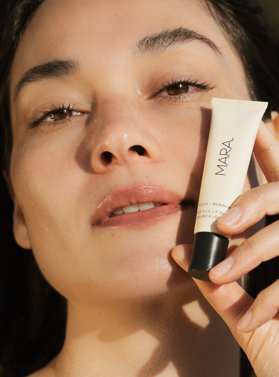 Woman holding a tube of Clear Sea Silk Lip Balm near her face