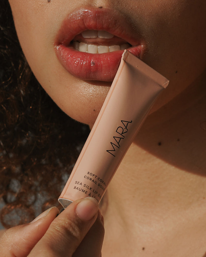 Model holding Soft Coral Sea Silk Lip Balm near lips | Mara Beauty