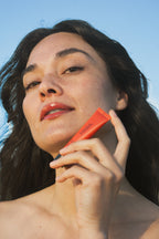 Person holding Sea Silk Lip Balm against a clear blue sky