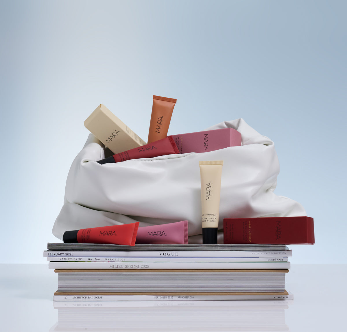 White tote bag filled with Sea Silk LIp Balm on a stack of magazines against a light blue background
