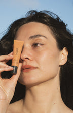 Woman holding a Sea Silk Lip Balm Sea Latte against her face with a clear blue sky background