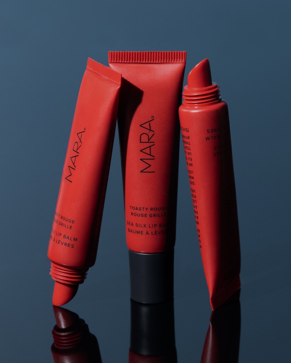 Three Toasty Rouge Sea Silk Lip Balm on blue background