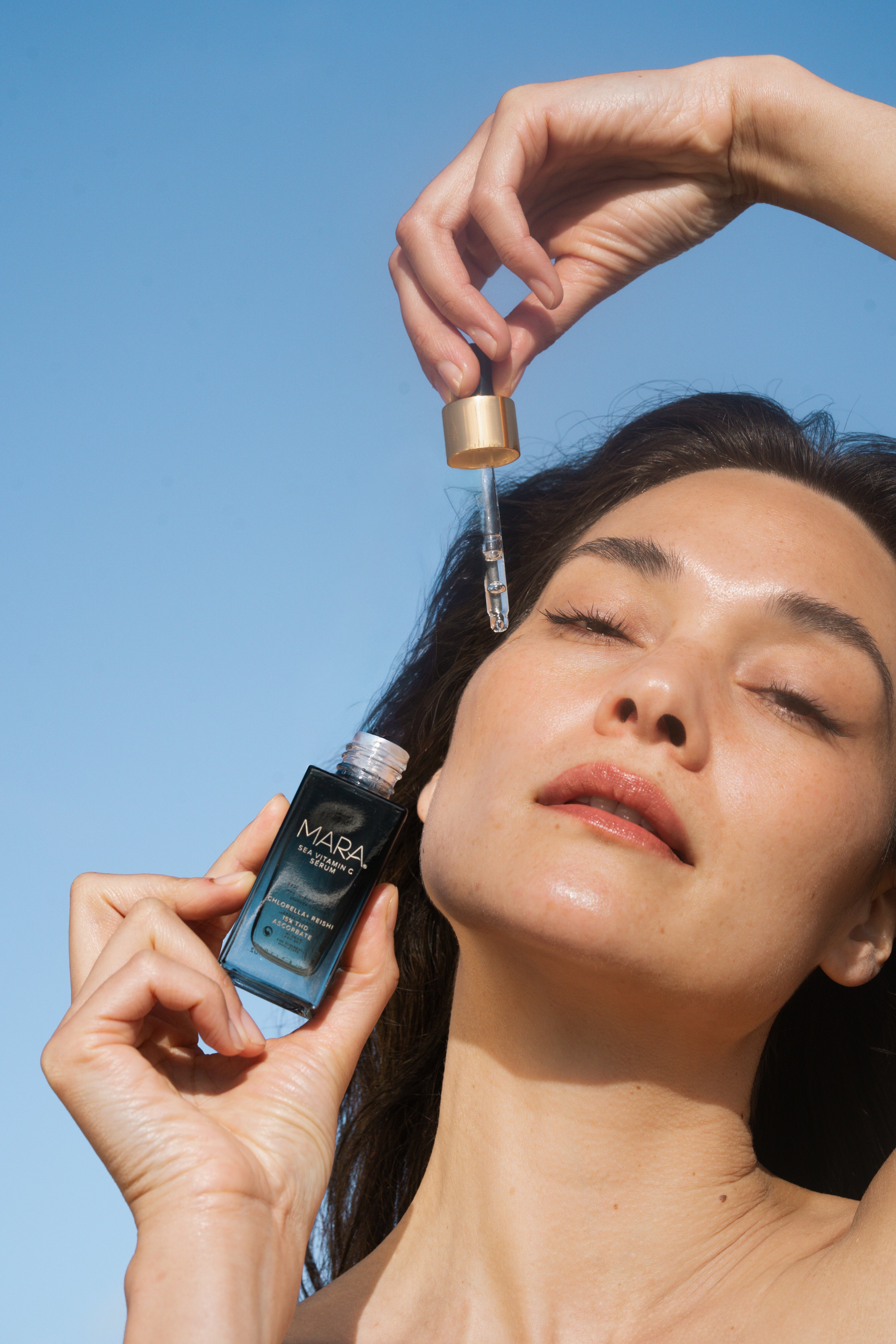 Model holding Sea Vitamin C Serum applying dropper to skin