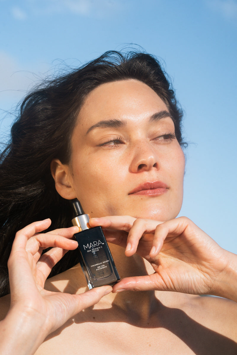 Woman holding Sea Vitamin C Serum against a clear blue sky.