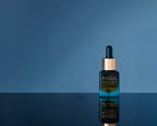 Universal Face Oil on a reflective surface with a blue background