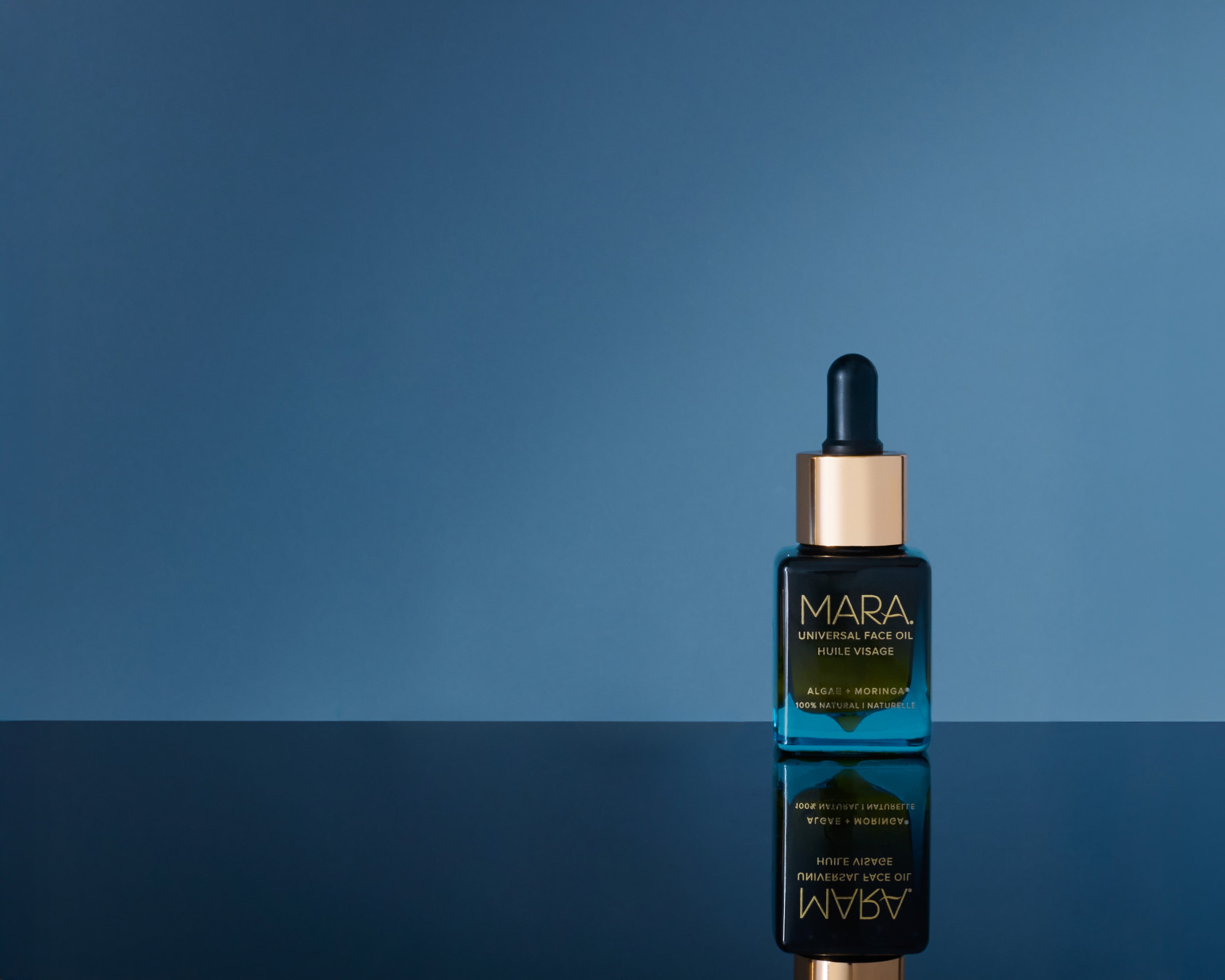 Universal Face Oil on a reflective surface with a blue background