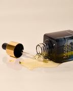 Universal Face Oil on side with a dropper spilling on a beige background