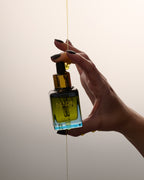 Hand holding Universal Face Oil  with a droplet of oil being released against a neutral background