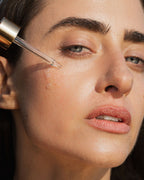 Close-up of a woman applying Universal Face Oil with a dropper to her face.