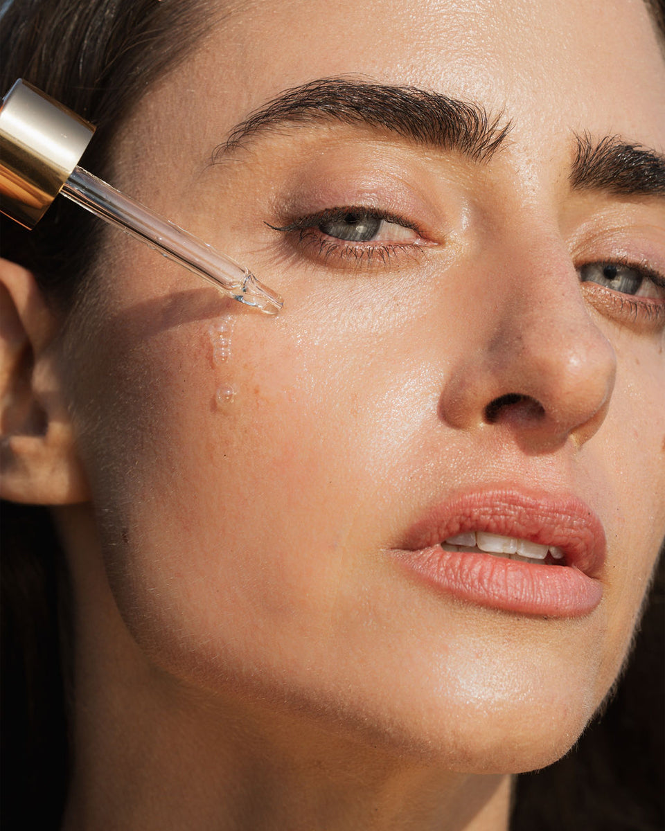Close-up of a woman applying Universal Face Oil with a dropper to her face.