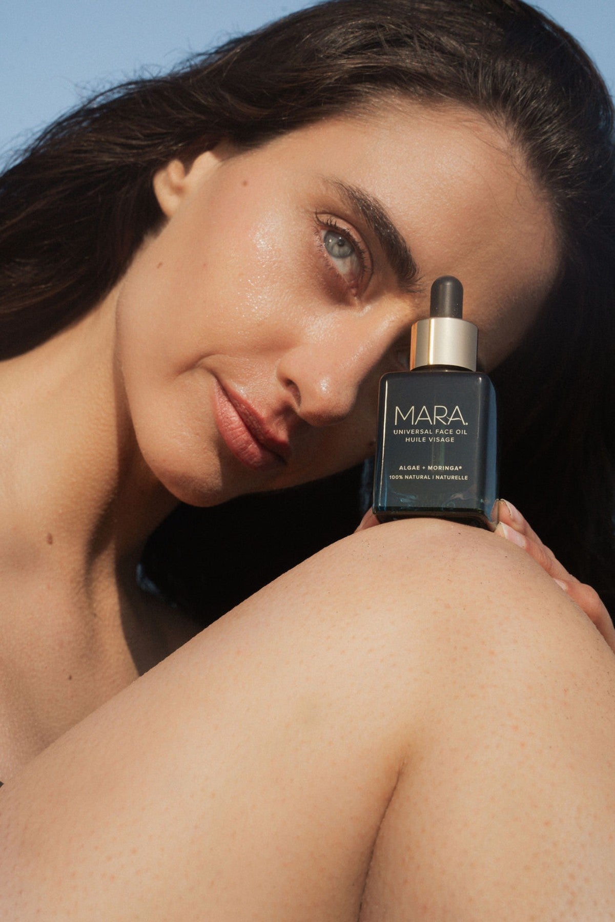 Model holding Universal Face Oil on knee