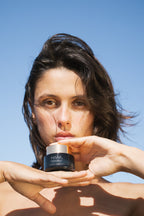 Woman holding a Volcanic Sea Clay Detox Masque against a clear blue sky