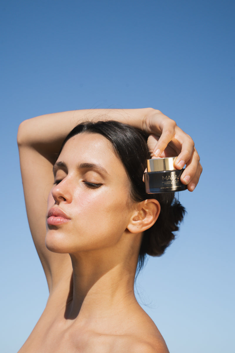 Woman holding Volcanic Sea Clay Detox Masque against a clear blue sky