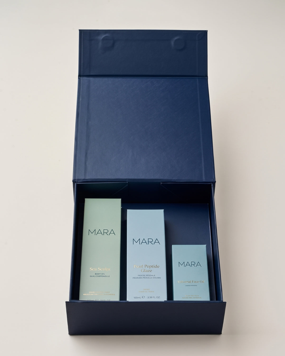 A navy blue gift box opened to reveal Sea Sculpt Body Oil, Pearl Peptide Glaze, Universal Face Oil.