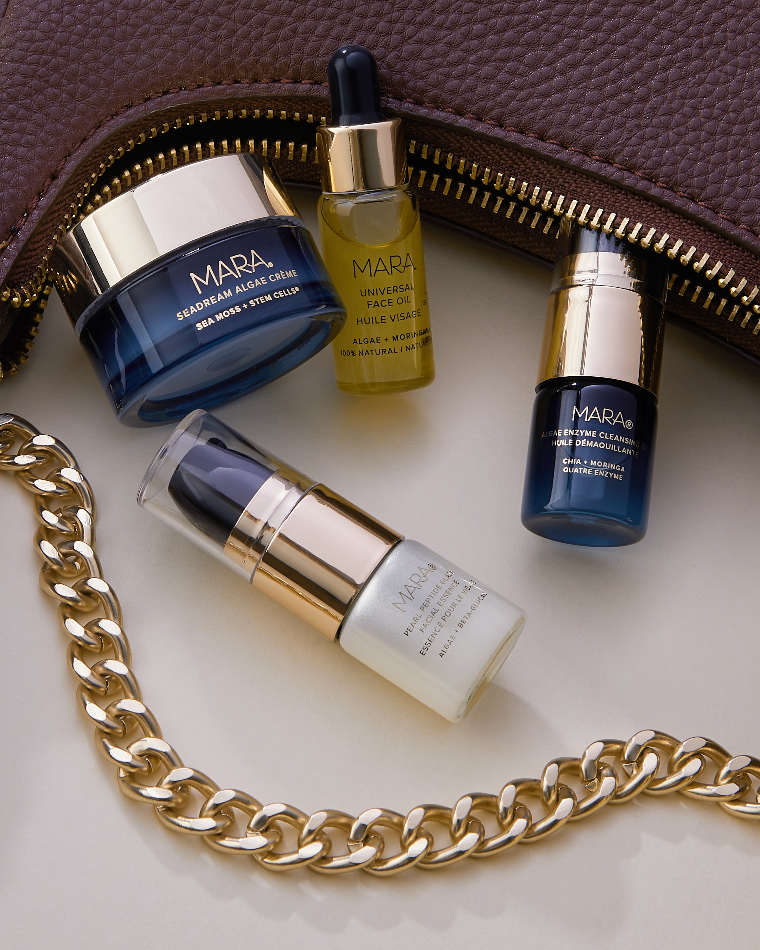 Deluxe Cleansing Oil, Pearl Peptide, Universal Oil, and Mini SeaDream spilling out of small burgundy purse with gold chain